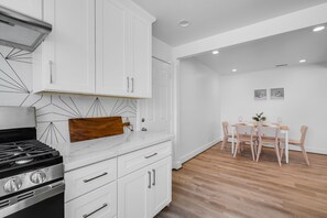 A modern kitchen with white cabinets, a wooden countertop, and a dining area with a table and chairs. - Comfortable 3 Bedroom House w/ AC + Free Wi-Fi (East Palo Alto)