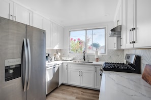 A modern kitchen with white cabinets, a stainless steel refrigerator, a built-in stove, and a window with a view of flowers.