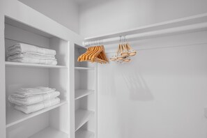 A white closet with shelves holding folded towels and a rack with hangers and shoes.