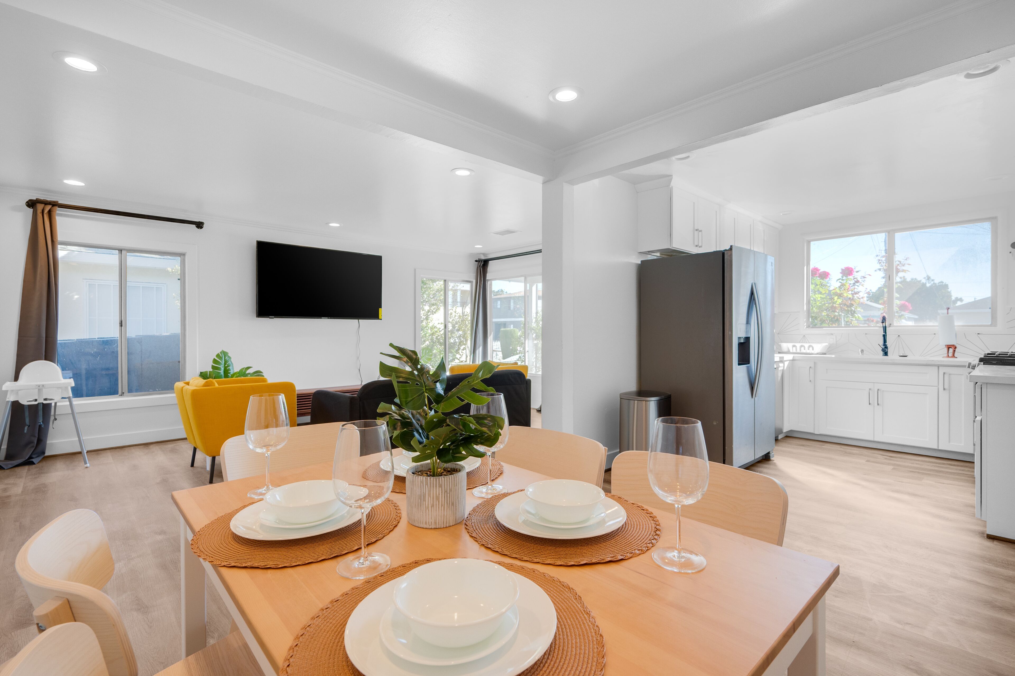 A modern kitchen with white cabinets, a stainless steel refrigerator, and a dining area with a wooden table set for four.