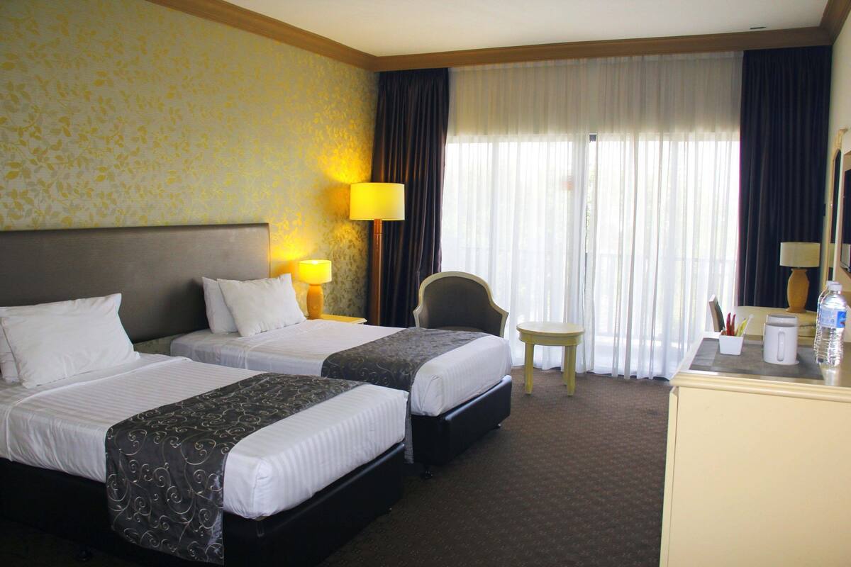 A hotel room with two beds, a desk, a chair, and a small table.