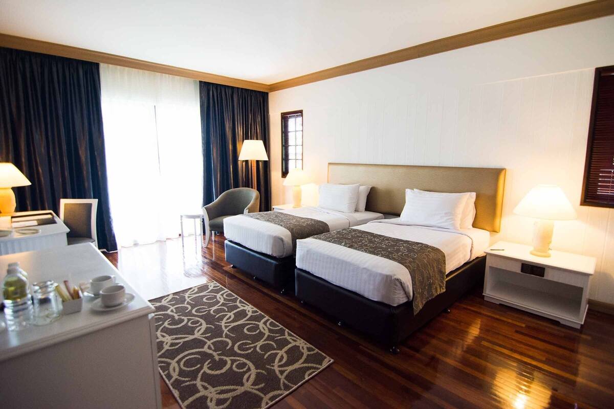 A hotel room with two beds, a desk, a chair, and a nightstand with lamps.