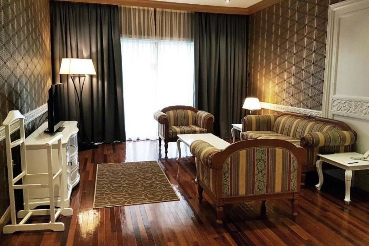 A room with a wooden floor, a sofa, a chair, a small table, a lamp, and a wardrobe.