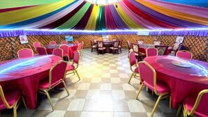 Un salón de banquetes con mesas y sillas redondas, piso a cuadros y cortinas decorativas.