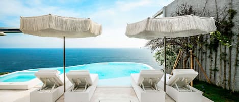 Una piscina al aire libre, sombrillas, sillones reclinables de piscina
