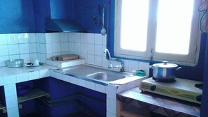 Une cuisine de taille réduite avec des murs recouverts de carreaux blancs, un évier, une fenêtre et une cuisinière.