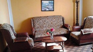 Un salon avec un canapé à motifs, deux fauteuils, une table basse en bois et un tableau encadré au mur.