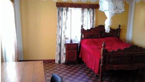 Une pièce avec un lit en bois, une table en bois, une chaise et une fenêtre avec des rideaux.