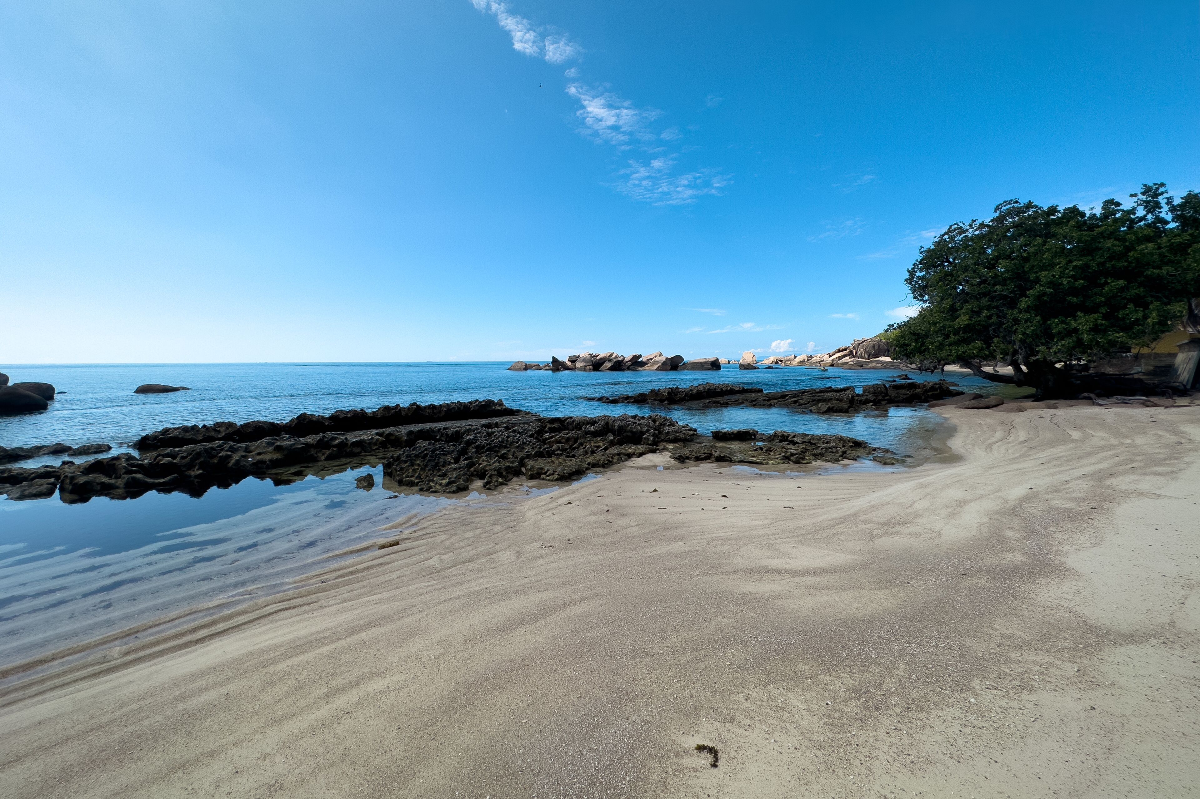 A beach with clear blue water, rocky outcrops, and a sandy shore.