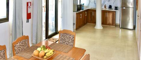 A dining area with a wooden table set for four, a fruit bowl, and a fire extinguisher on the wall.