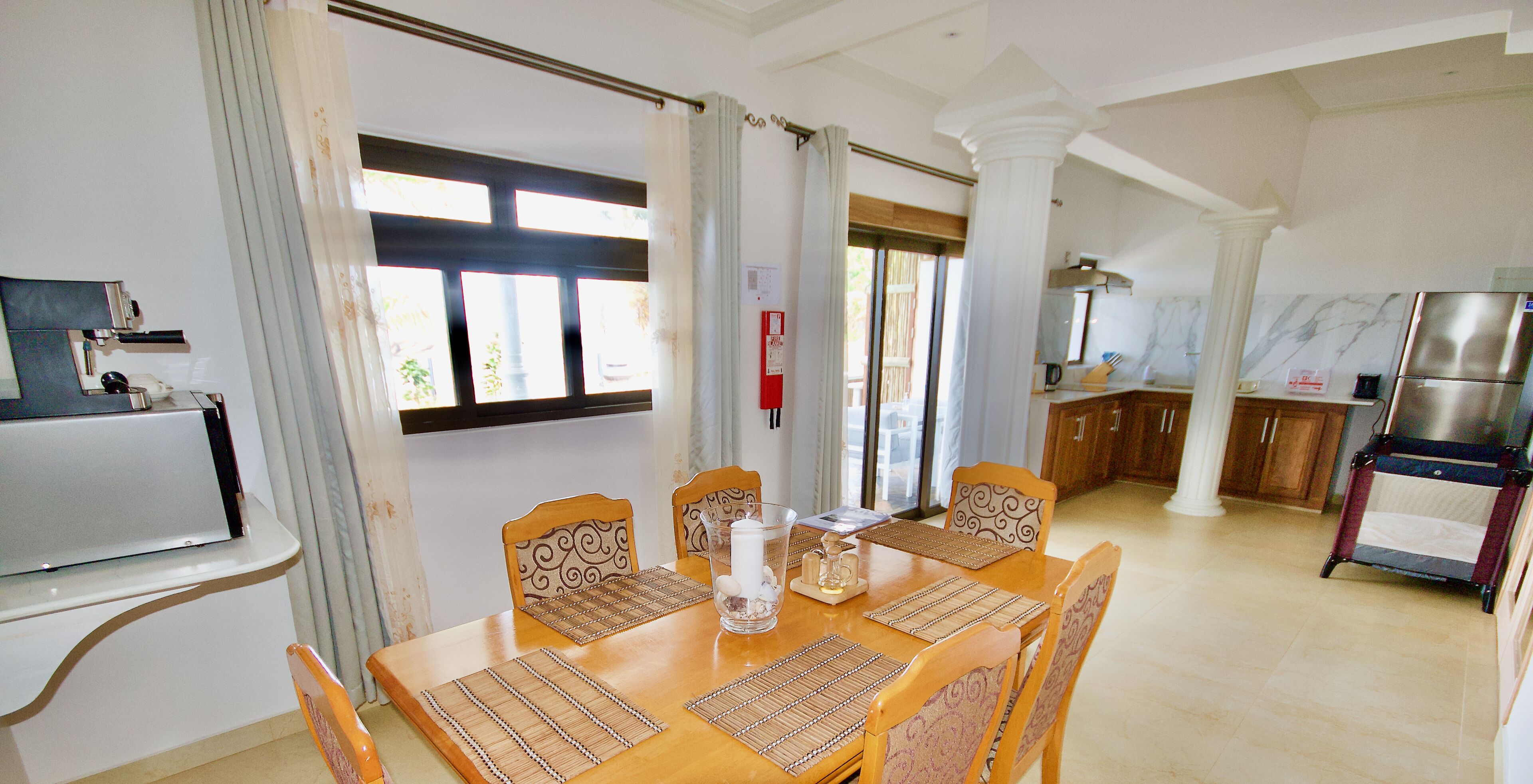 Un comedor con mesa de madera, sillas y un refrigerador al fondo.