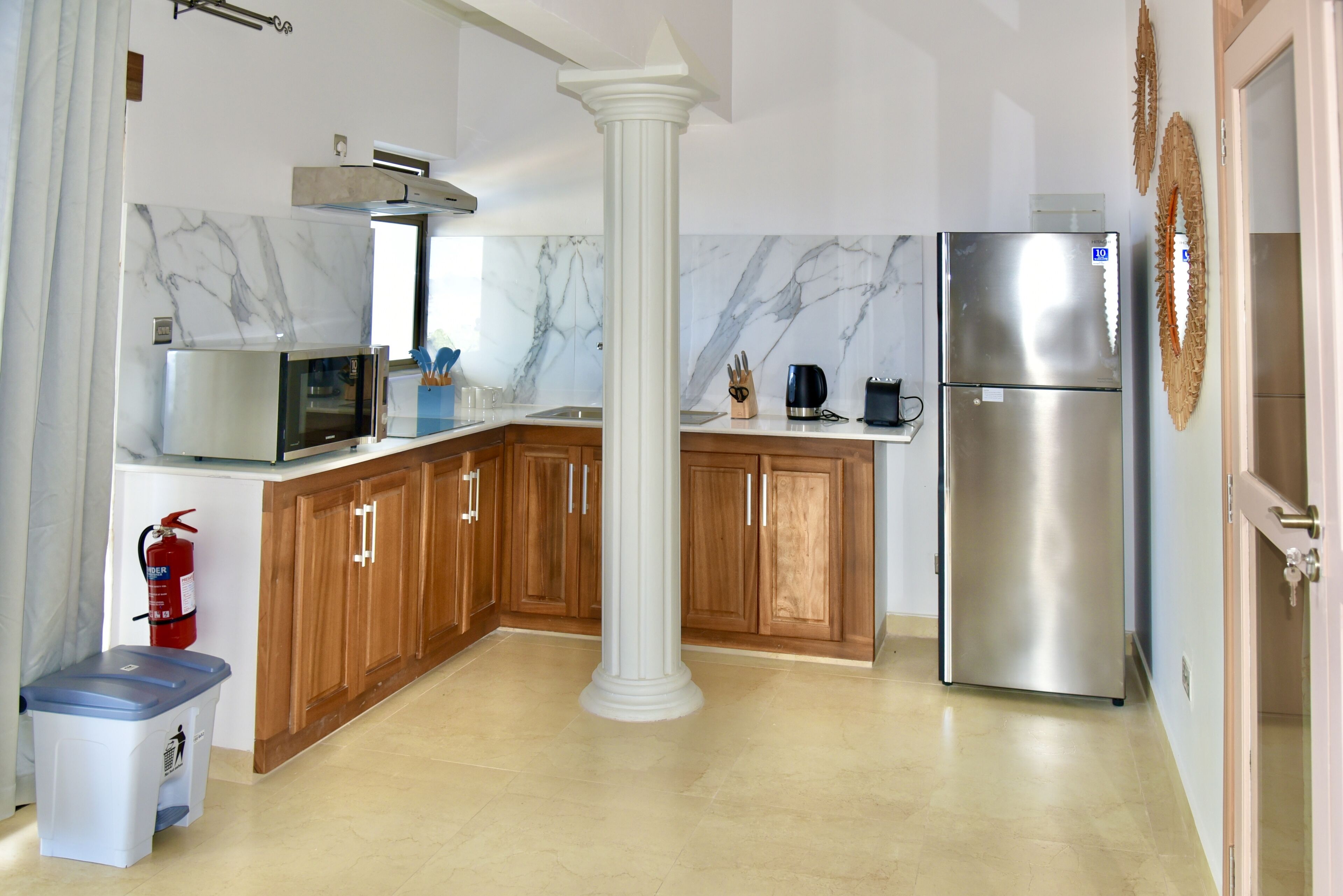 A kitchen with marble backsplash, wooden cabinets, a stainless steel refrigerator, and a fire extinguisher.