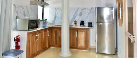 A kitchen with marble backsplash, wooden cabinets, a stainless steel refrigerator, and a fire extinguisher.