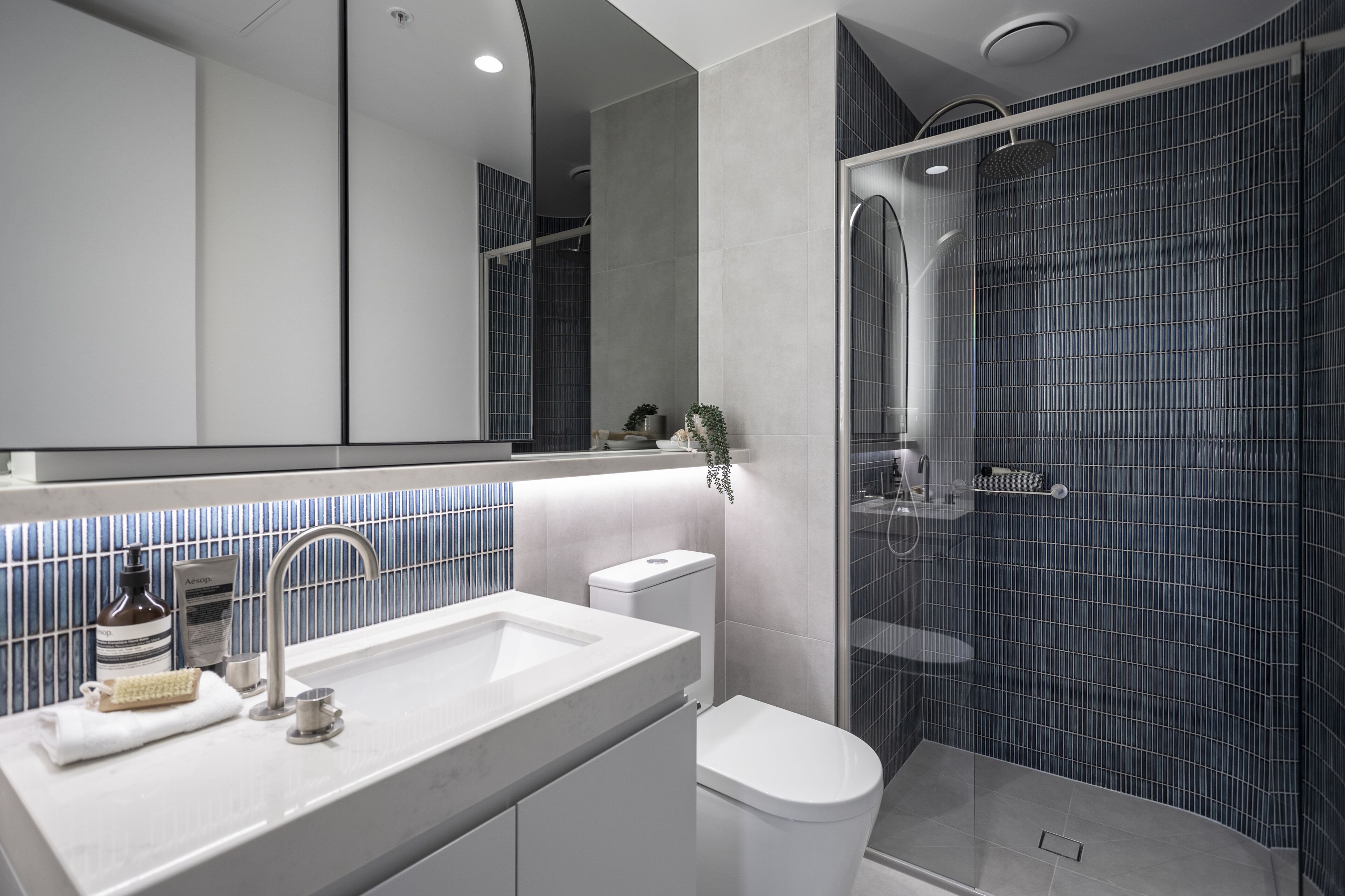 Une salle de bain moderne avec un lavabo blanc, des toilettes et une douche séparée par une paroi en verre.