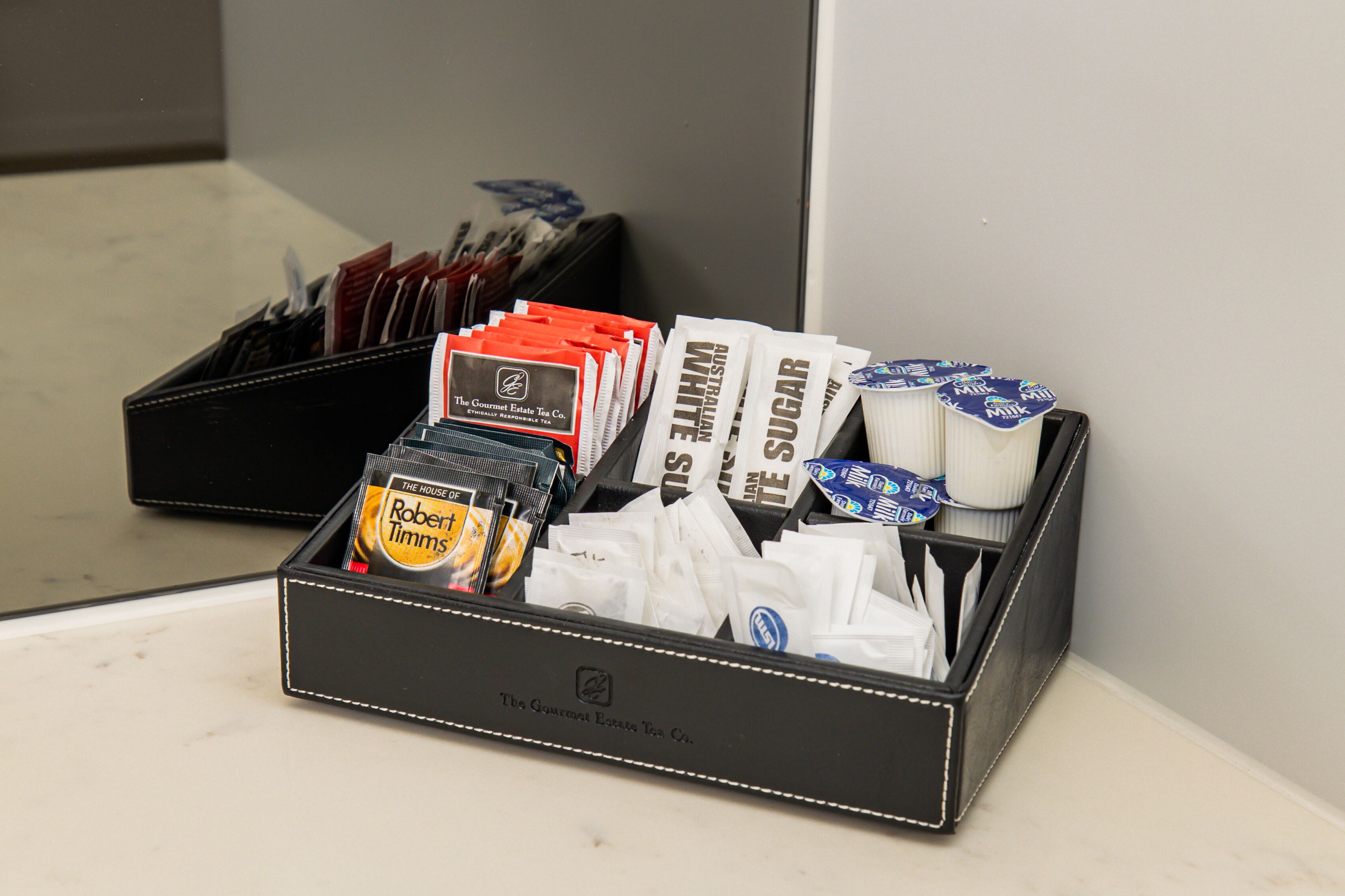 A black leather box filled with various tea packets and sugar packets.