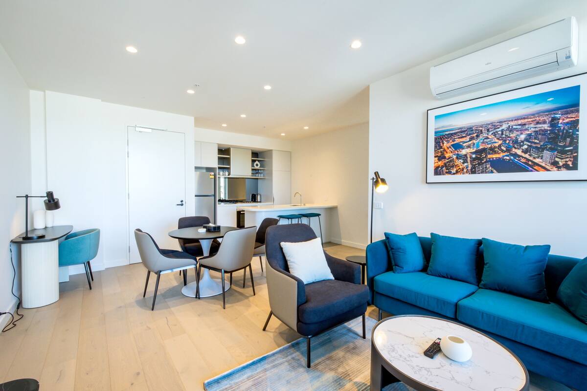 A modern living room with a blue sofa, a coffee table, and a dining area with chairs and a table.