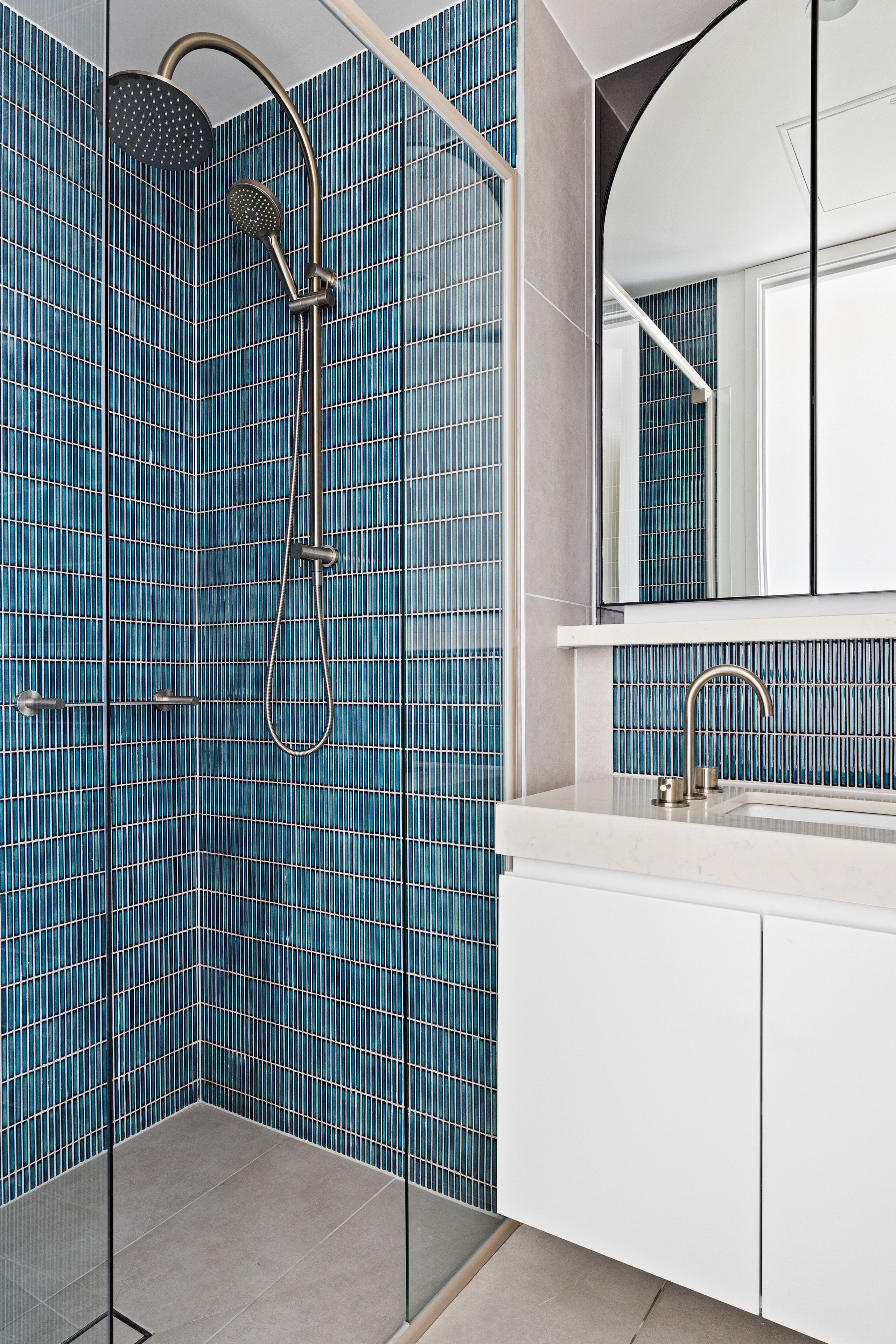 Uma casa de banho moderna com paredes azulejadas em azul, uma cabine de duche envidraçada e um lavatório branco com espelho.
