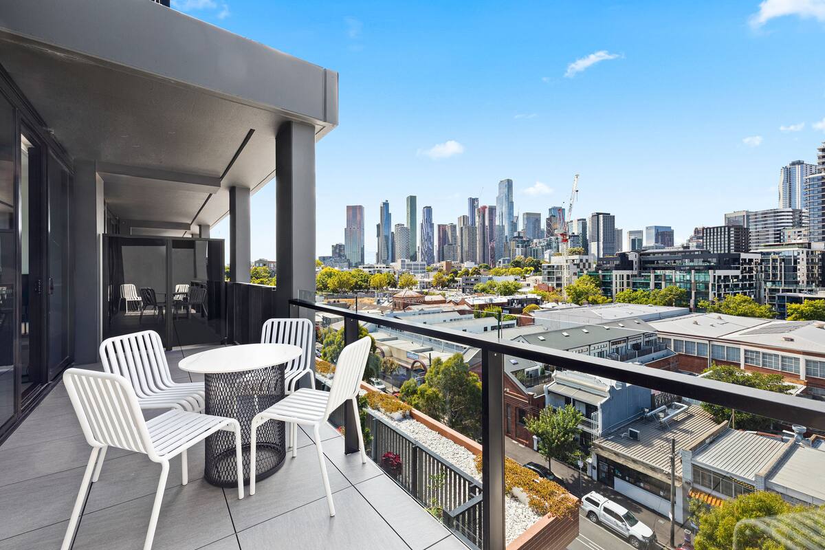 A balcony with a city view, white chairs, and a round table.