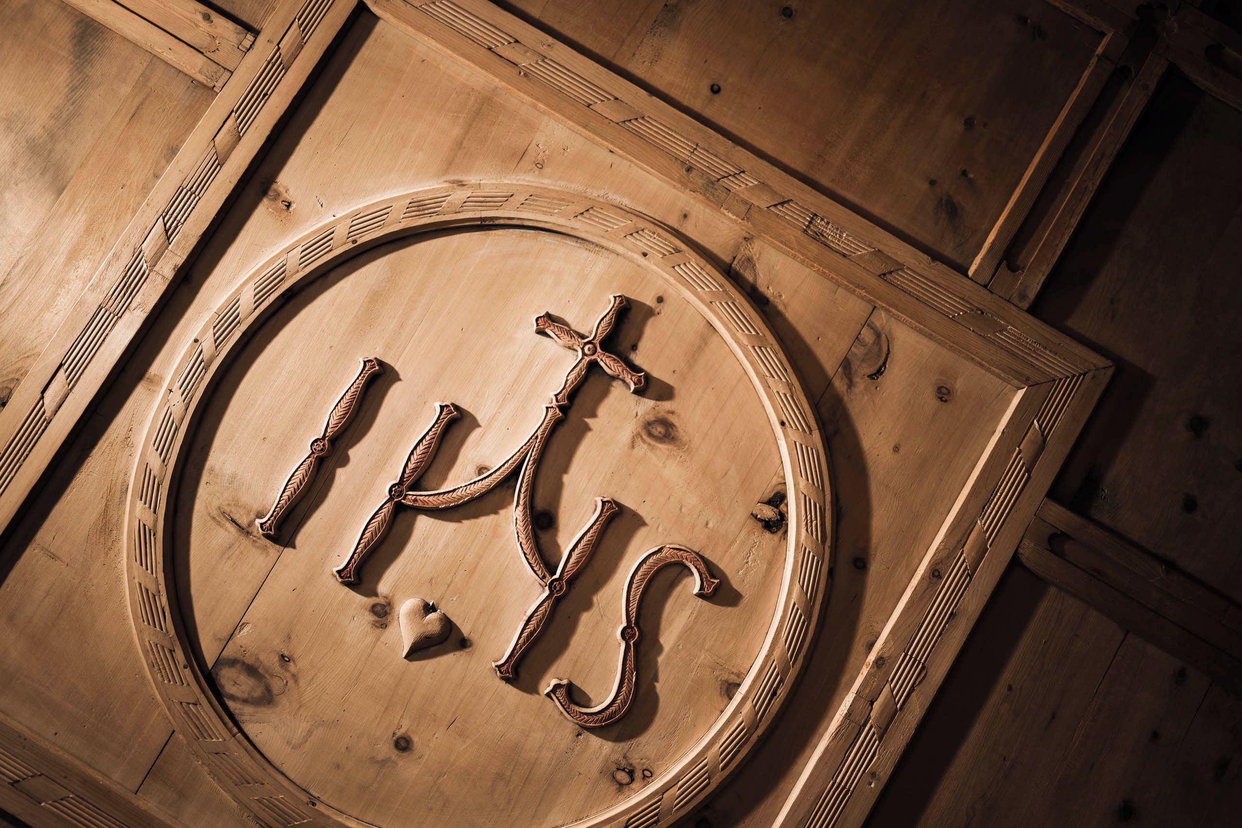 A wooden sign with the letters 'IHS' and a cross, indicating a religious symbol.