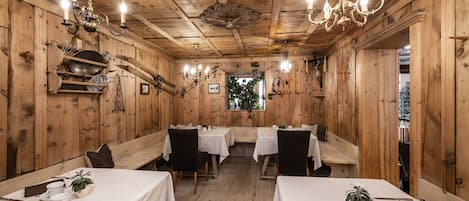 A wooden interior with tables set for dining, a chandelier, and a window with plants.