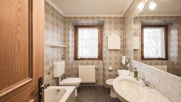 A bathroom with a toilet, sink, and bathtub. There are two windows with curtains, a towel rack, and a mirror.