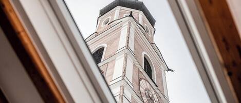 Vista a través de una ventana de un edificio con una torre de reloj, que presenta una cúpula y una cruz en la parte superior.
