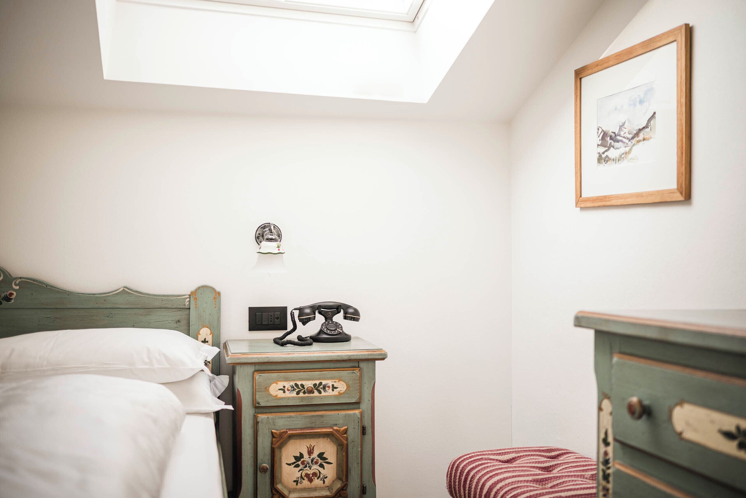 A bedroom with a bed, a dresser, a telephone, and a framed picture on the wall.