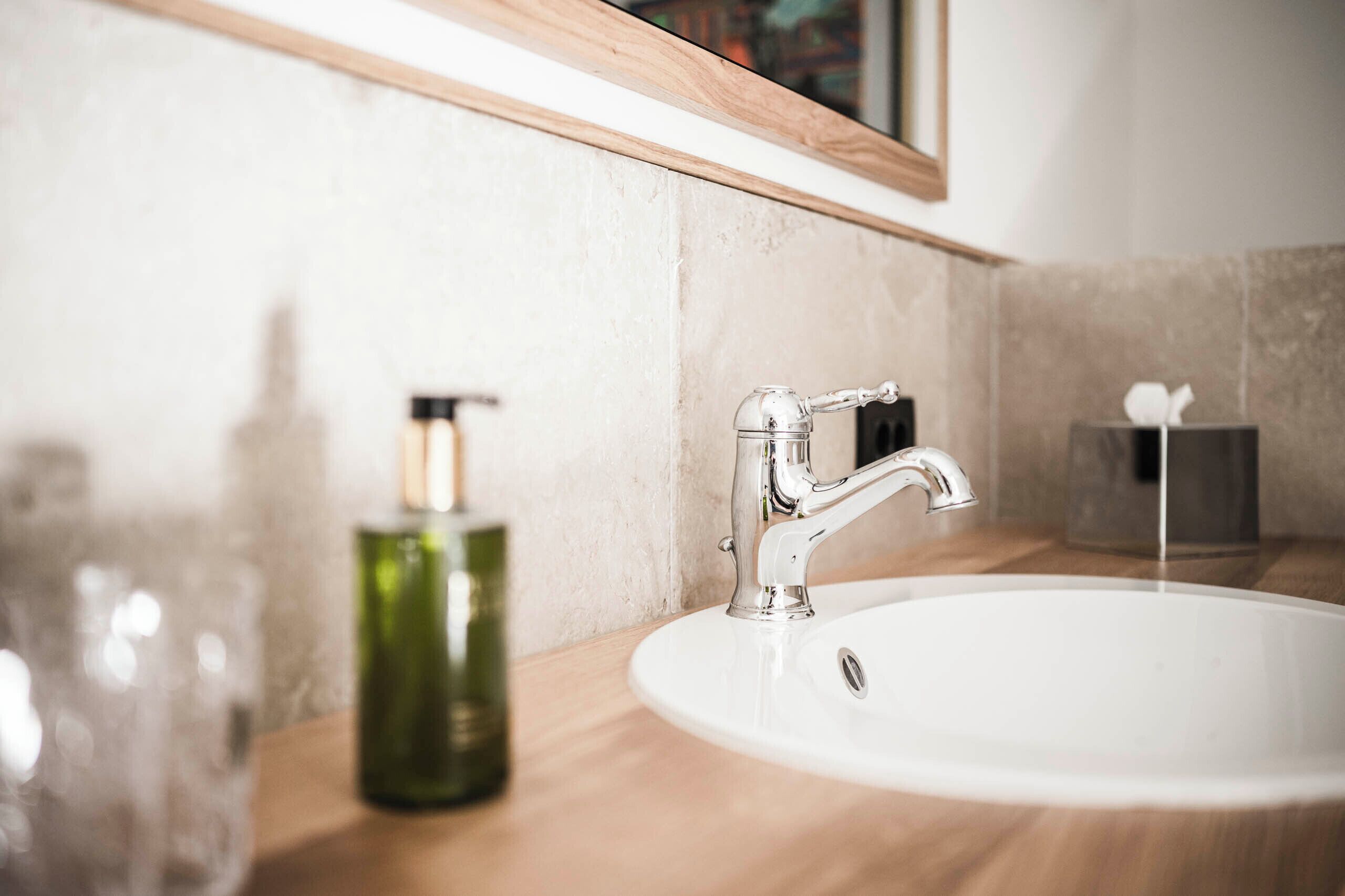 A bathroom sink with a modern faucet, a green bottle, and a tissue box on the counter.