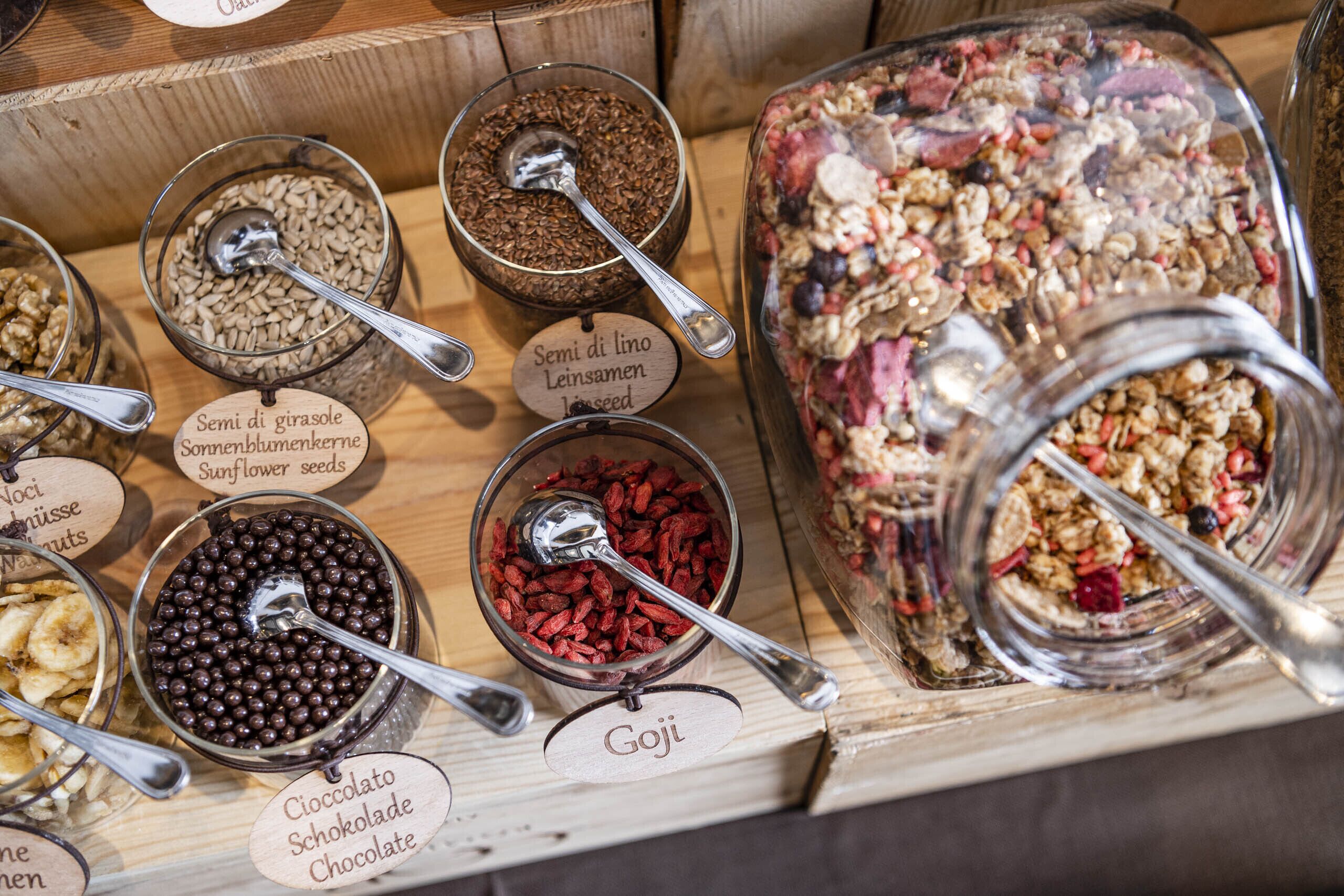 A variety of food items in glass containers with labels, including sunflower seeds, goji berries, and chocolate.