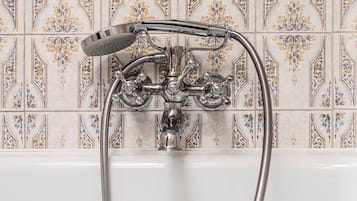 Un baño con una bañera blanca, un cabezal de ducha y un grifo. La pared está revestida con un diseño floral.