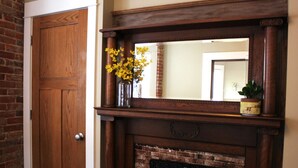 A wooden door, a fireplace with a mirror above it, and a vase with yellow flowers.