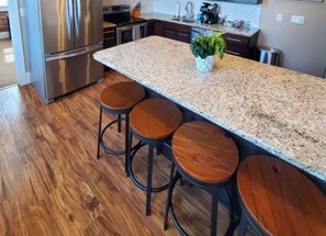 A kitchen with a granite countertop, stainless steel appliances, and wooden stools.