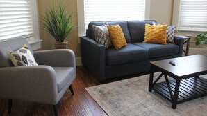 A living room with a grey sofa, a grey armchair, and a coffee table. There is a potted plant and a rug on the floor.