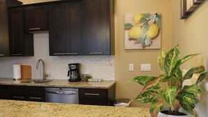 A kitchen with dark wooden cabinets, a granite countertop, a coffee maker, and a potted plant.