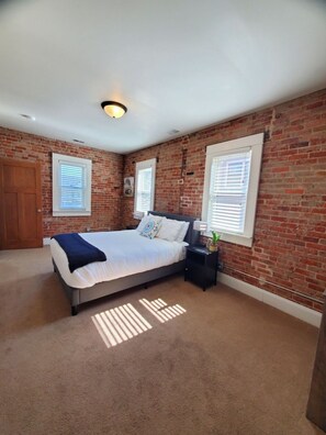 A bedroom with a brick wall, a bed, a nightstand, and a window.