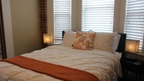 A neatly made bed with white bedding and an orange throw blanket, flanked by two bedside lamps.