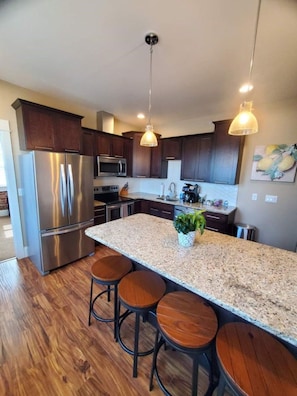 A modern kitchen with a central island, stainless steel appliances, and wooden bar stools.