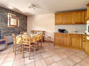 Cozinha com armários de madeira, piso ladrilhado e mesa de jantar posta para quatro pessoas.