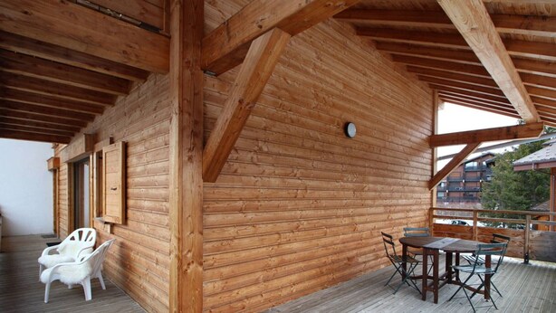 A wooden cabin with a deck, a dining table with chairs, and a white chair.