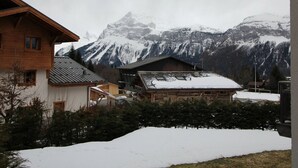 A wooden building with a sloped roof, surrounded by snow-covered ground and mountains in the background.