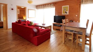 A cozy living room with a red sofa, wooden dining table, and a TV.