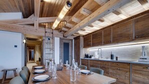 A wooden dining table with chairs, a kitchen with wooden cabinets, and a modern light fixture. - Spacious apartment with balcony and parking in La Rosière (Montvalezan-La Rosière)