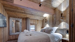A wooden-paneled bedroom with a large bed, a mirror, a window, and a wall-mounted light fixture. - Spacious apartment with balcony and parking in La Rosière (Montvalezan-La Rosière)