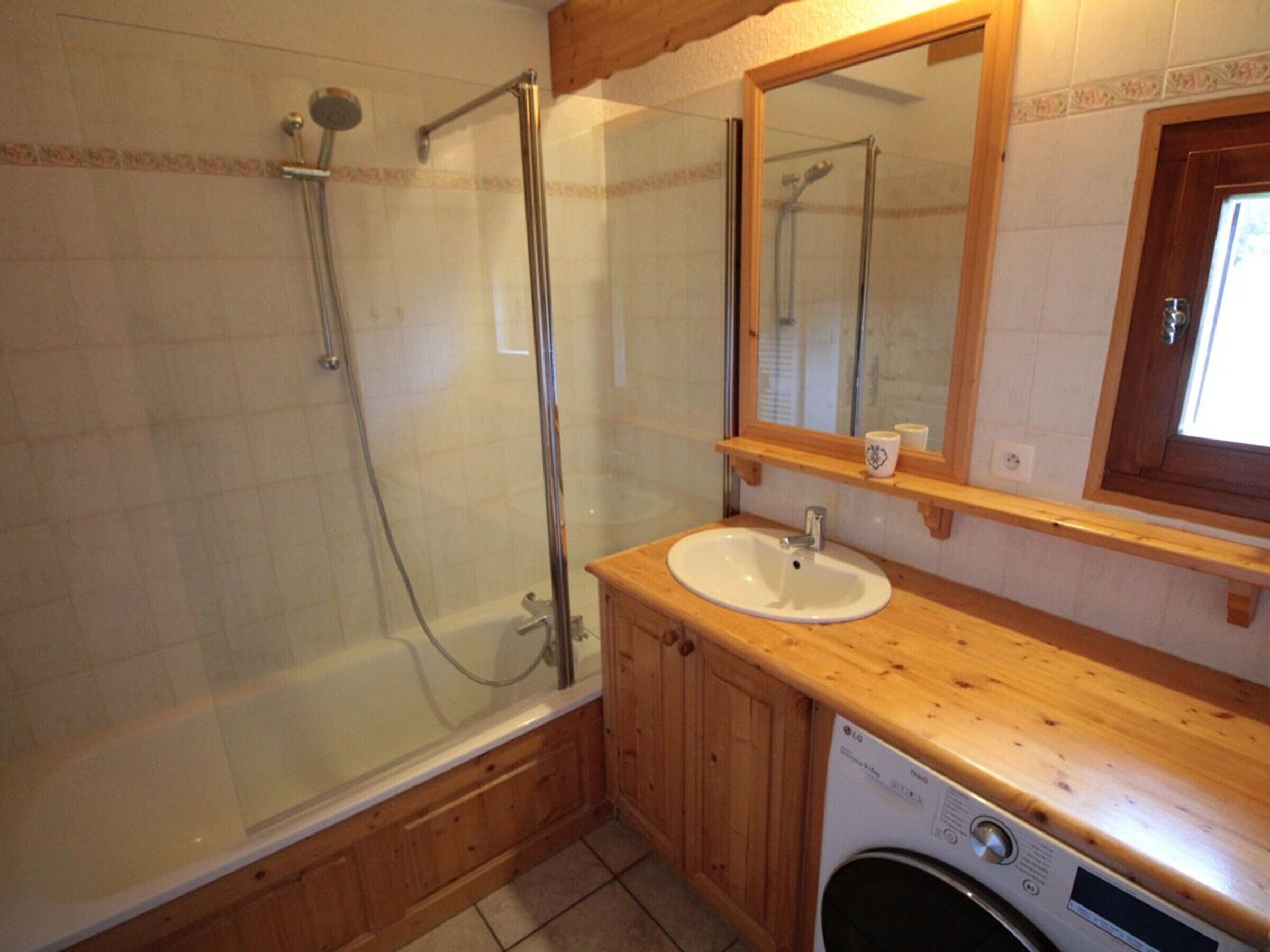 A bathroom with a glass-enclosed shower, a wooden vanity with a sink, and a washing machine.