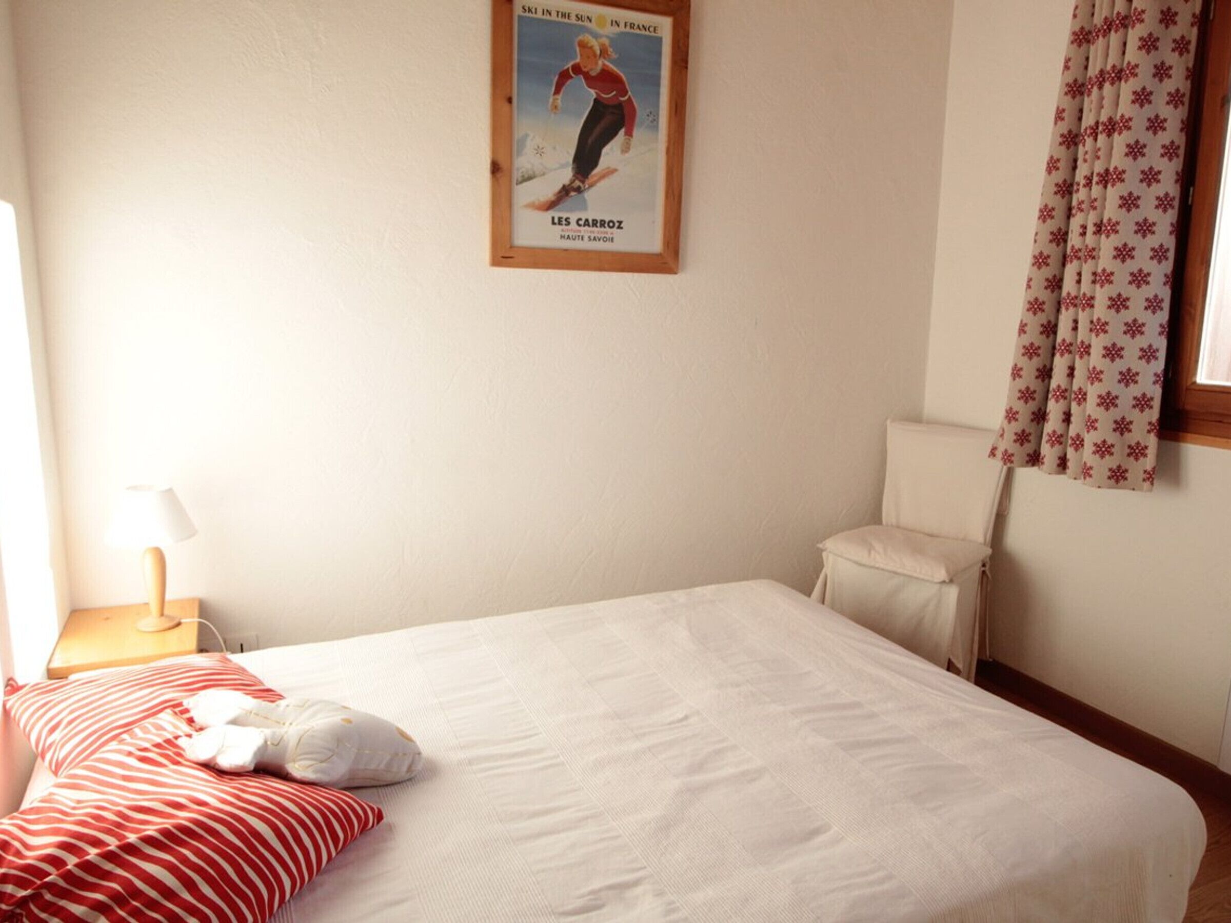 Ein Hotelzimmer mit einem Bett, einem Nachttisch, einer Lampe, einem Fenster mit Vorhängen und einem Bild an der Wand.