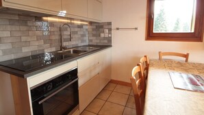 Een compacte keuken met een modern design, met een ingebouwde oven, een kookplaat en een spoelbak. Er is een eethoek met een tafel en stoelen, en een raam zorgt voor natuurlijk licht.