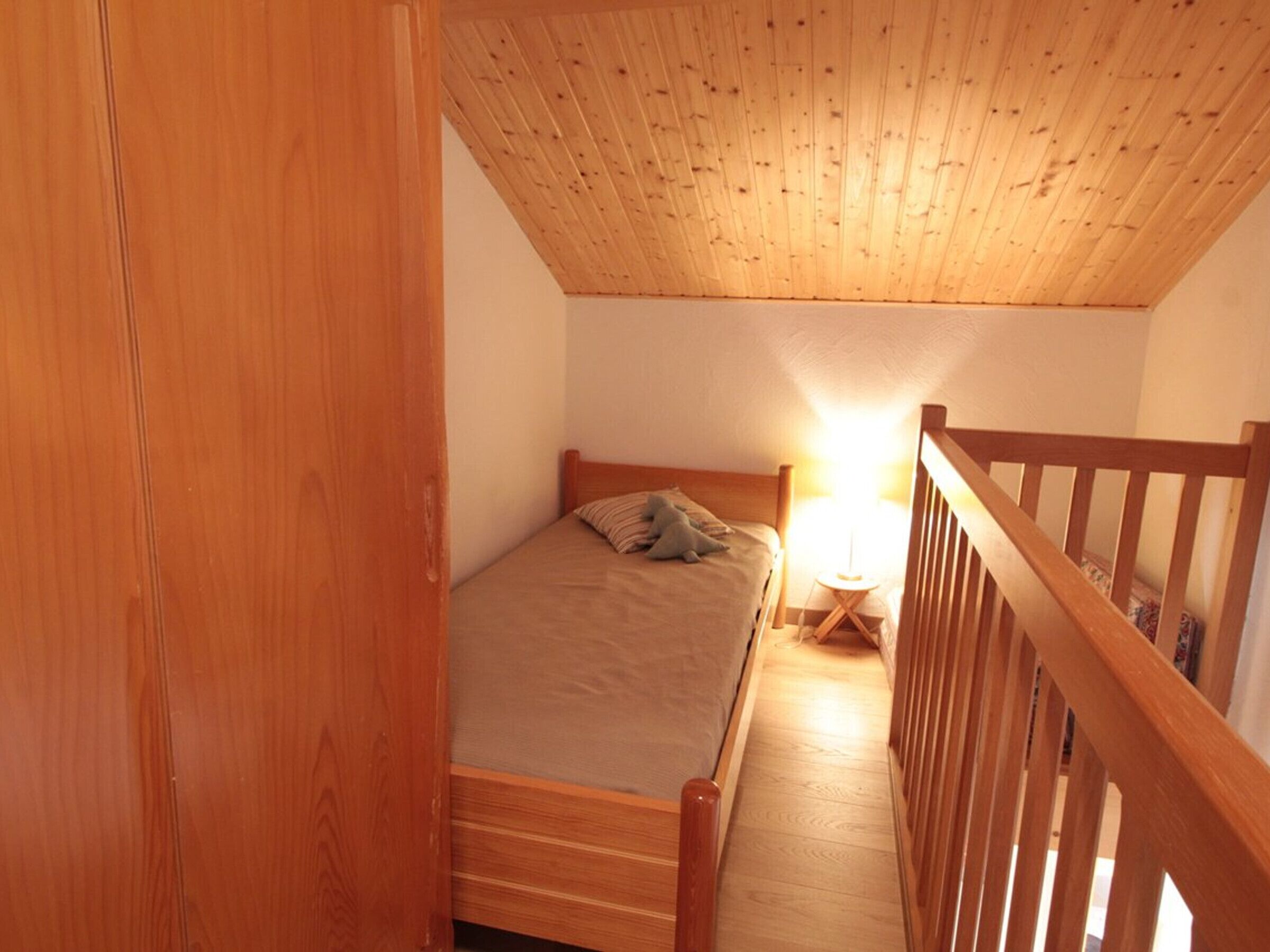 Une chambre avec un plafond en bois, un lit, une table de chevet et une balustrade en bois.