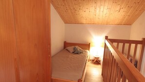 Een slaapkamer met een houten plafond, een bed, een nachtkastje en een houten leuning.