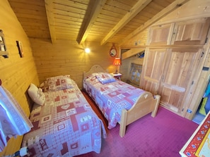 Quarto de madeira acolhedor, com duas camas, uma mesa de cabeceira, um abajur e um guarda-roupa.