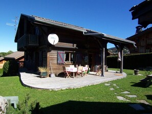 Une maison en bois dotée d’un balcon, d’une antenne parabolique et d’un petit espace extérieur aménagé avec des tables et des chaises.